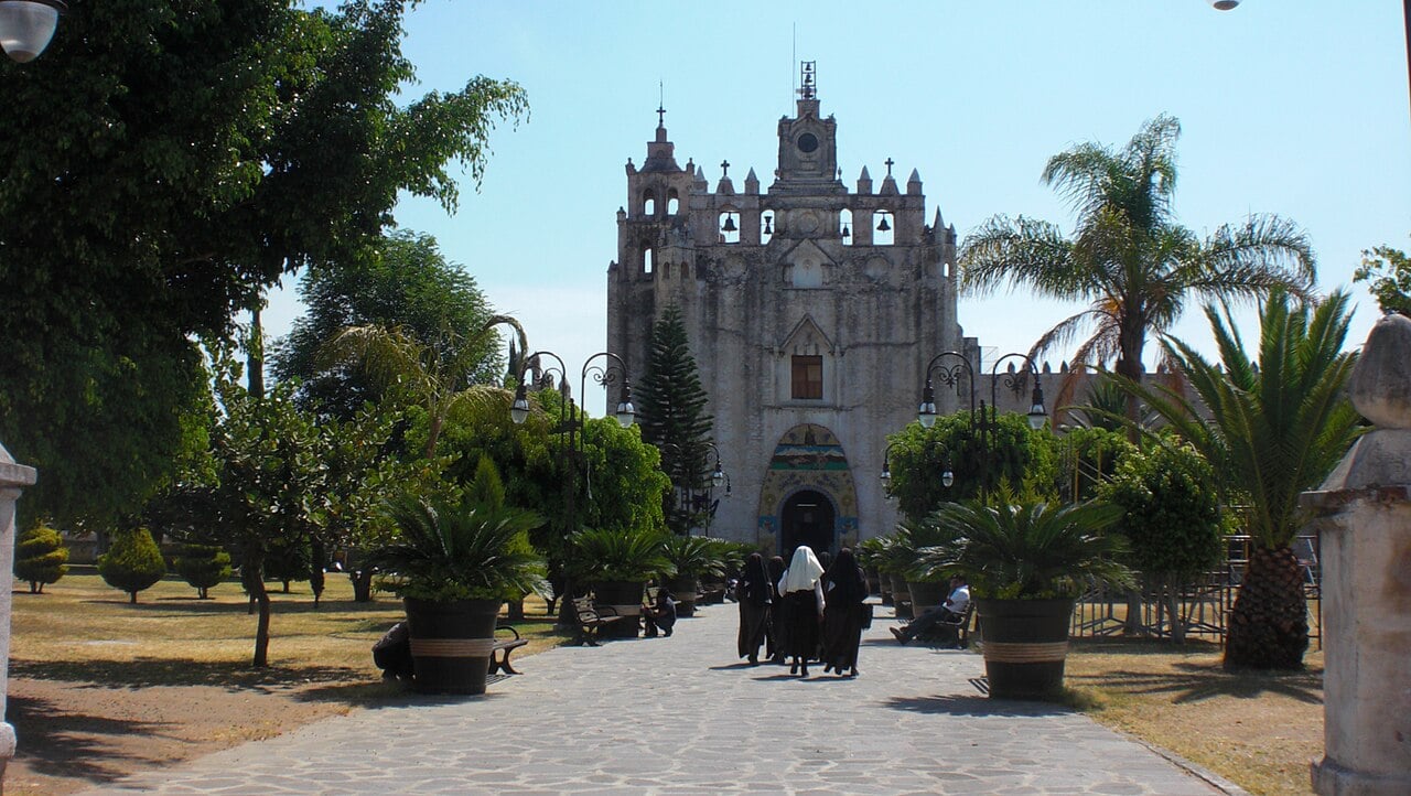 Women in religious habits walk along a paved path towards the stone former convent of San Mateo in Atlatlahucan, Morelos