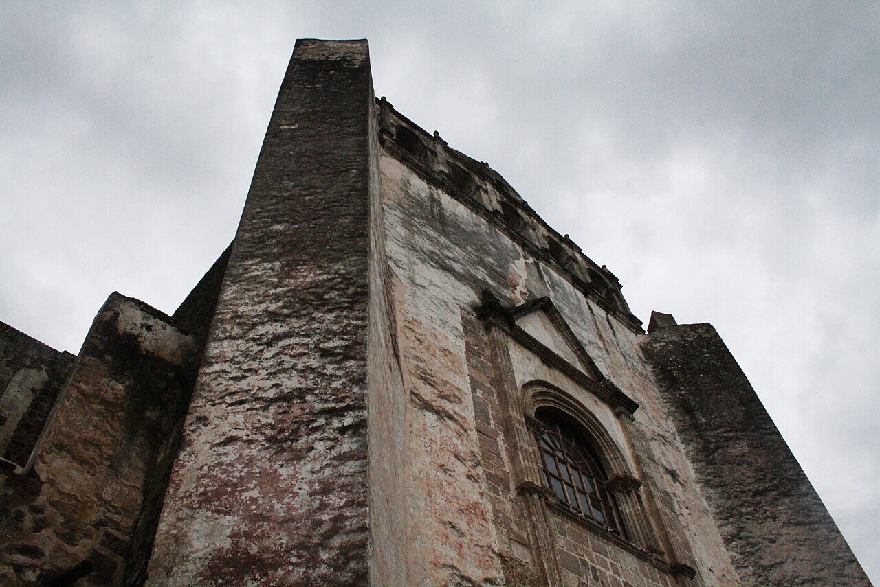 Weathered stone facade of the San Juan Bautista church in Tlayacapan, Morelos, under a grey sky