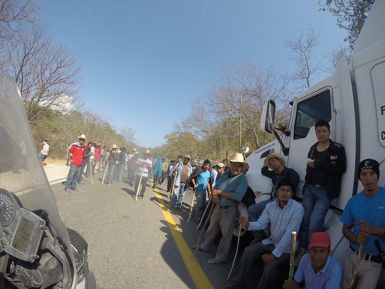 Protesters stand along a mountain highway in Oaxaca beside a parked white semi-truck cab