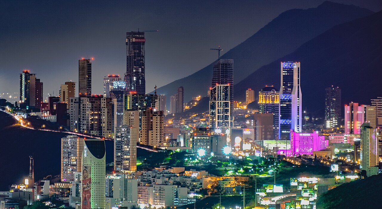 Night view of the Monterrey skyline in northern Mexico with lit office towers below a dark mountain ridge
