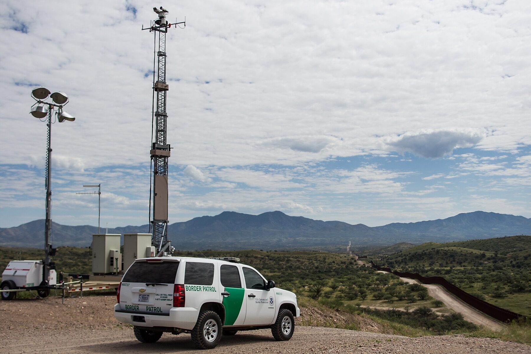 A US Border Patrol vehicle beside a surveillance tower on a hill overlooking the border barrier near Nogales, Arizona