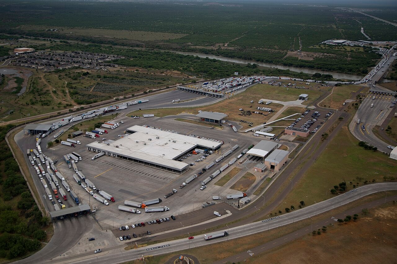 Aerial view of the World Trade Bridge cargo crossing at Laredo, Texas, with rows of trucks waiting at inspection lanes beside the Rio Grande