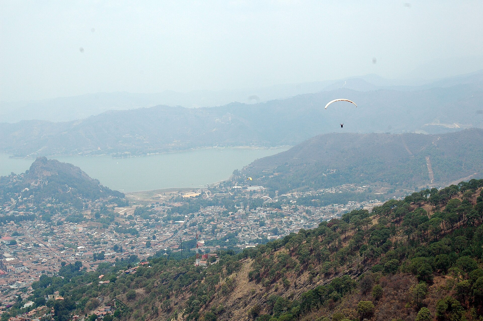 Aerial view of Valle de Bravo and its reservoir with a paraglider overhead