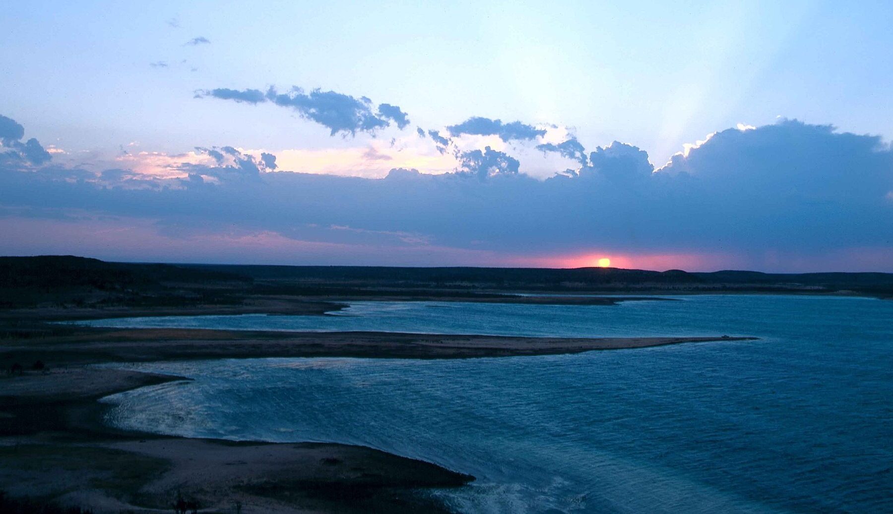 Wide view of Amistad Reservoir on the Rio Grande at sunset, with dark shoreline and a pink and blue sky over the water