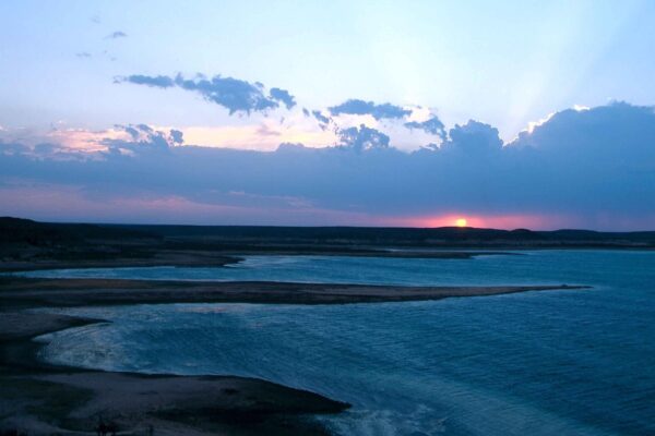 Wide view of Amistad Reservoir on the Rio Grande at sunset, with dark shoreline and a pink and blue sky over the water