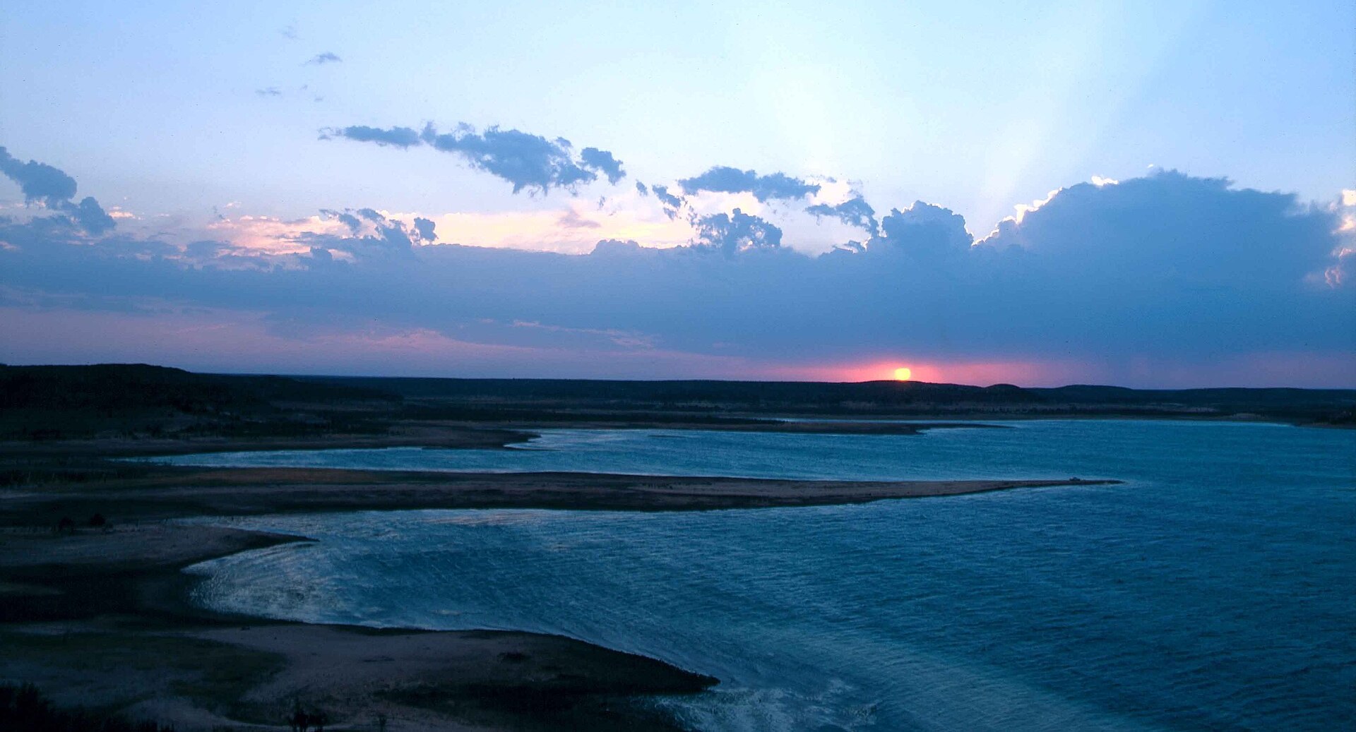 Wide view of Amistad Reservoir on the Rio Grande at sunset, with dark shoreline and a pink and blue sky over the water