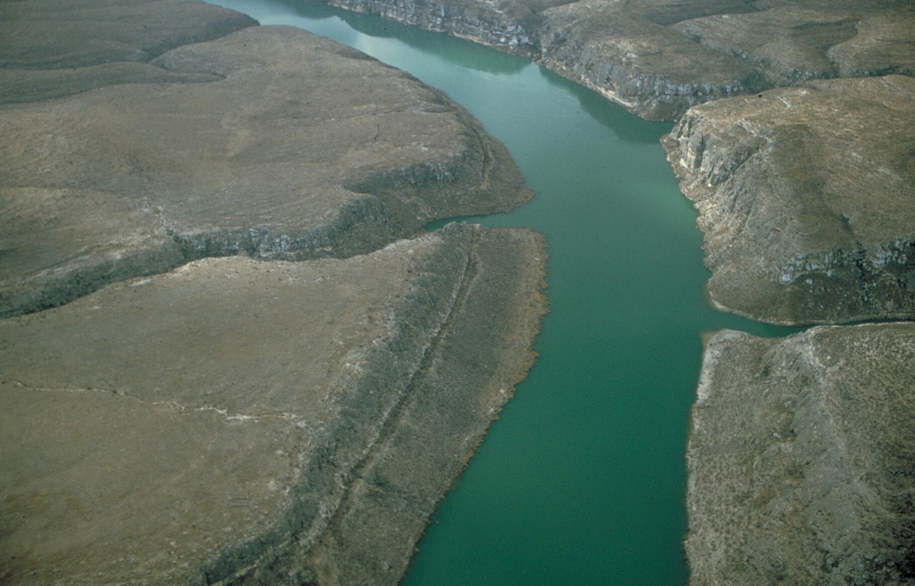 Aerial view of green-blue river water winding between rocky bluffs and brush-covered plateaus at Amistad National Recreation Area, Texas