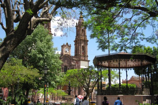 The main square of Zamora, Michoacán, with the cathedral tower and a wrought-iron bandstand under jacaranda trees