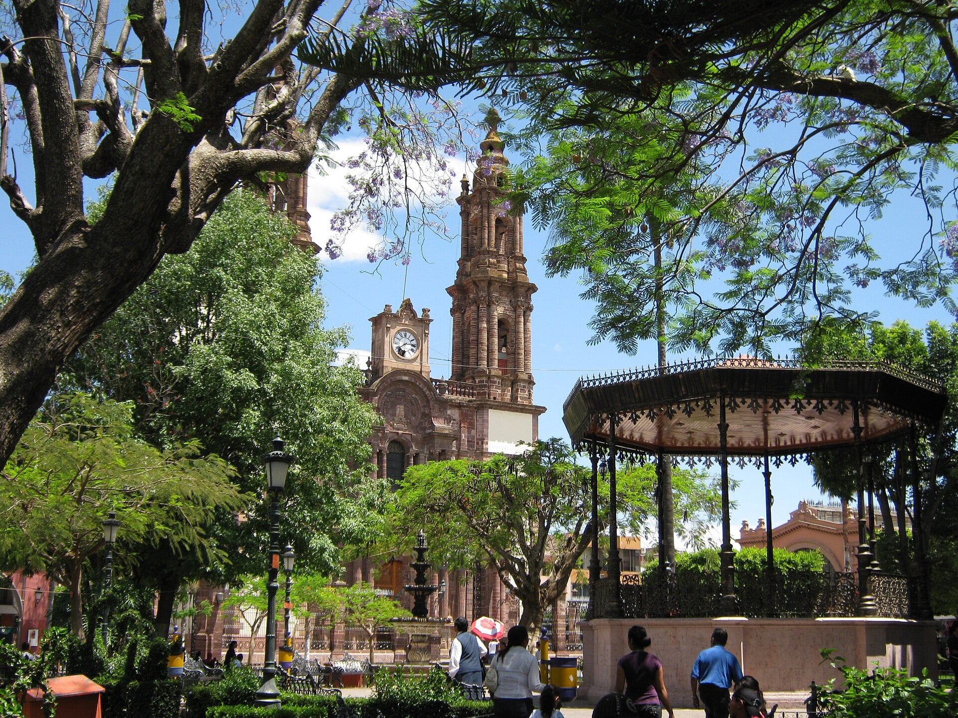 The main square of Zamora, Michoacán, with the cathedral tower and a wrought-iron bandstand under jacaranda trees