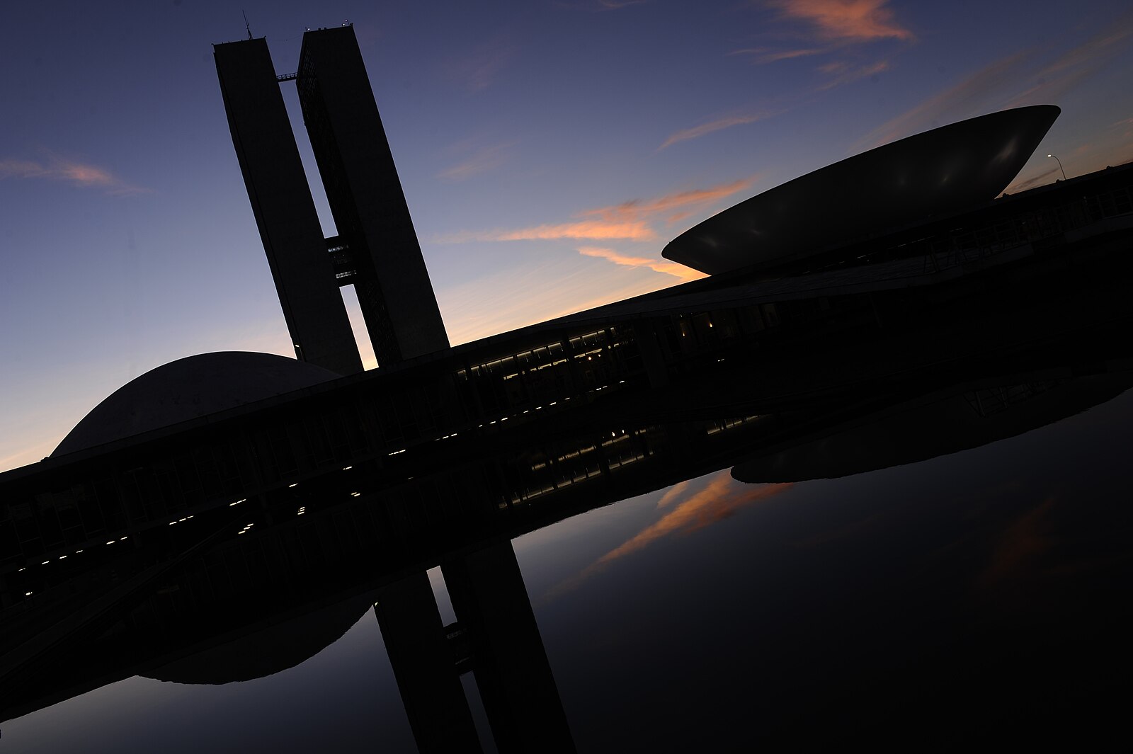 The twin office towers and domed chambers of the National Congress in Brasilia at dawn, reflected in water