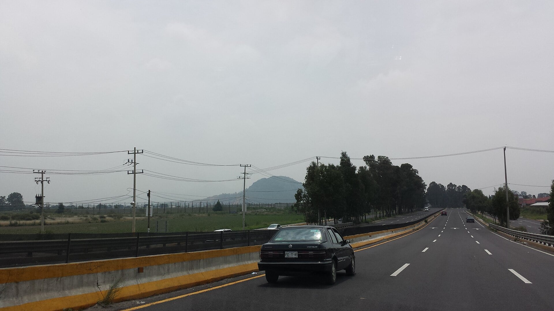 A car on a divided multilane highway between Mexico City and Puebla, with fields and a hill under a hazy sky
