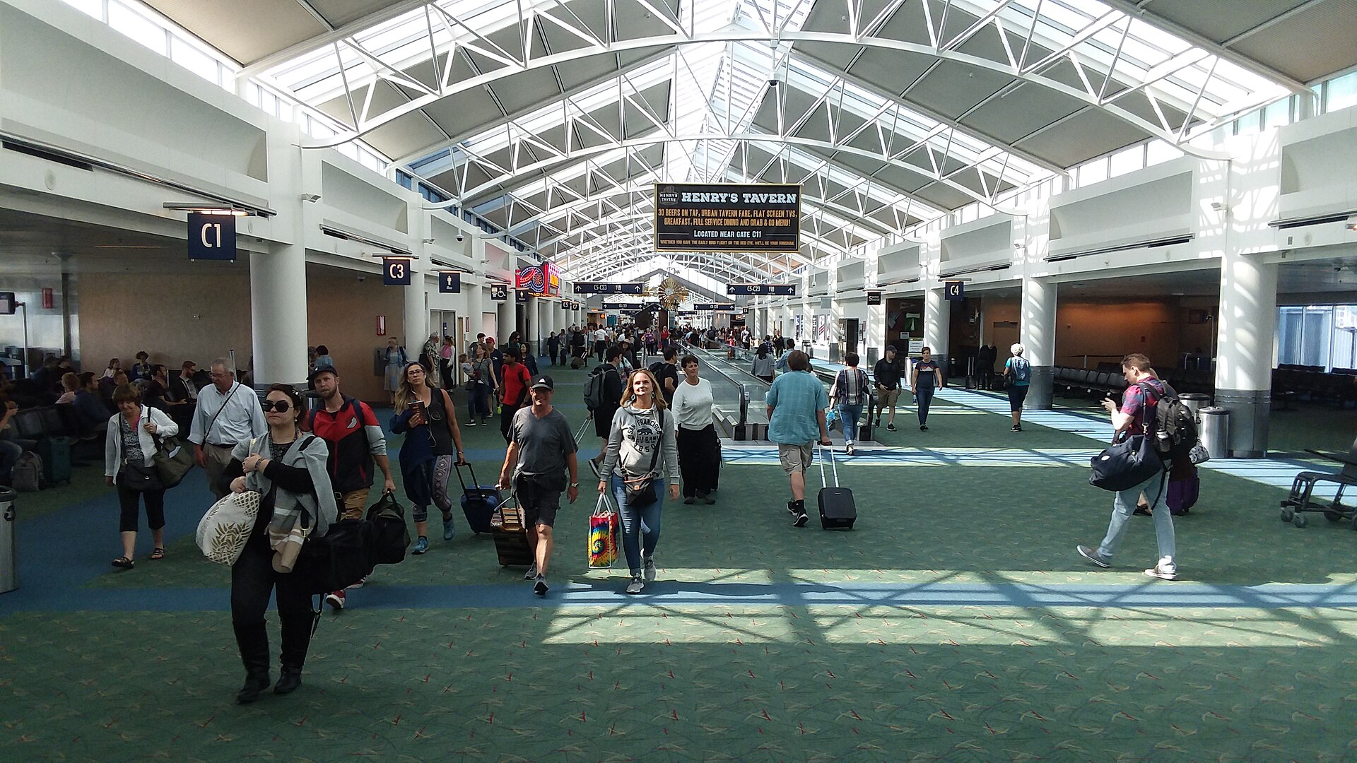 Travellers with wheeled bags walking through a bright, glass-roofed concourse at Portland International Airport