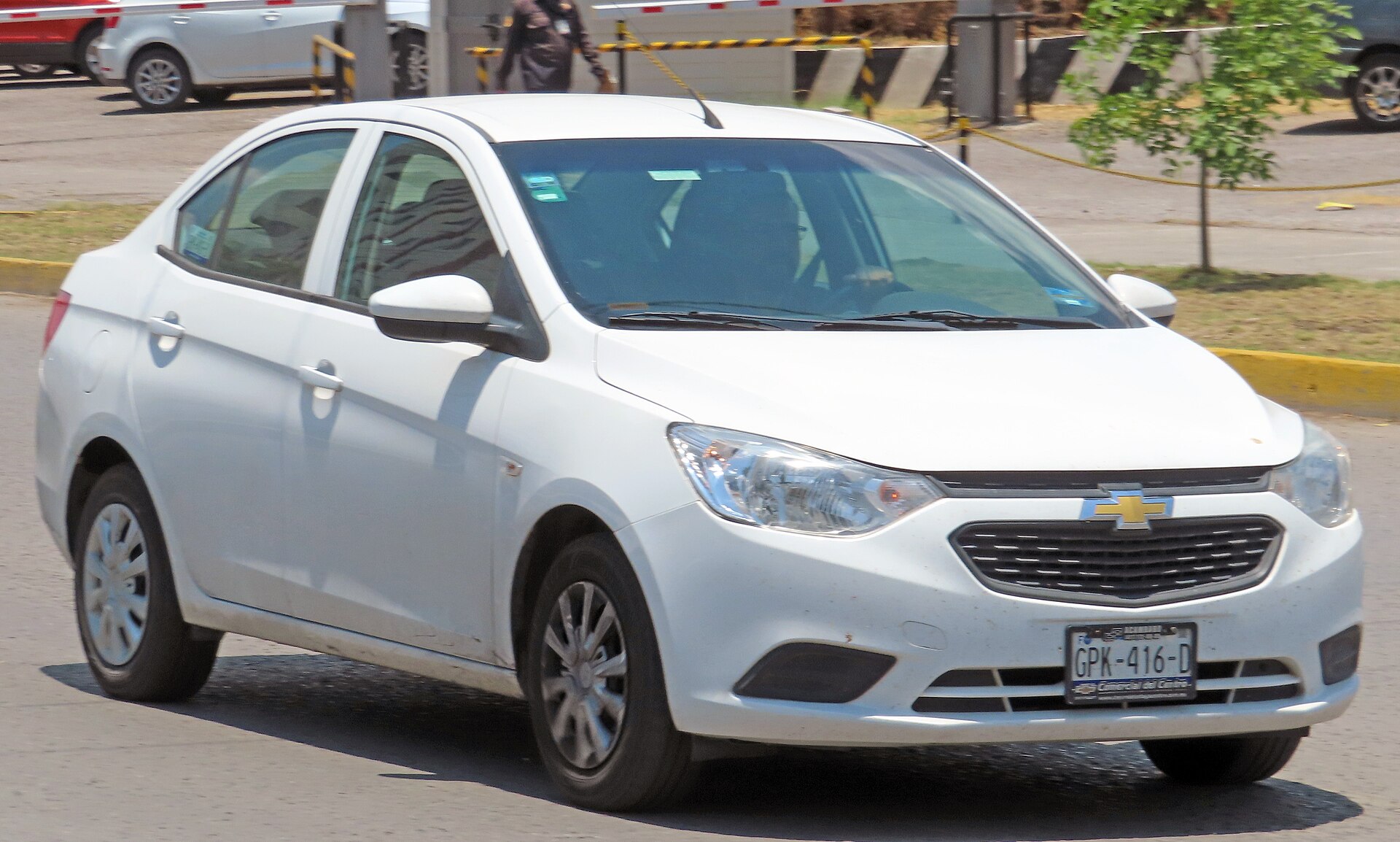 A white Chevrolet Aveo sedan with Mexican plates driving on a road