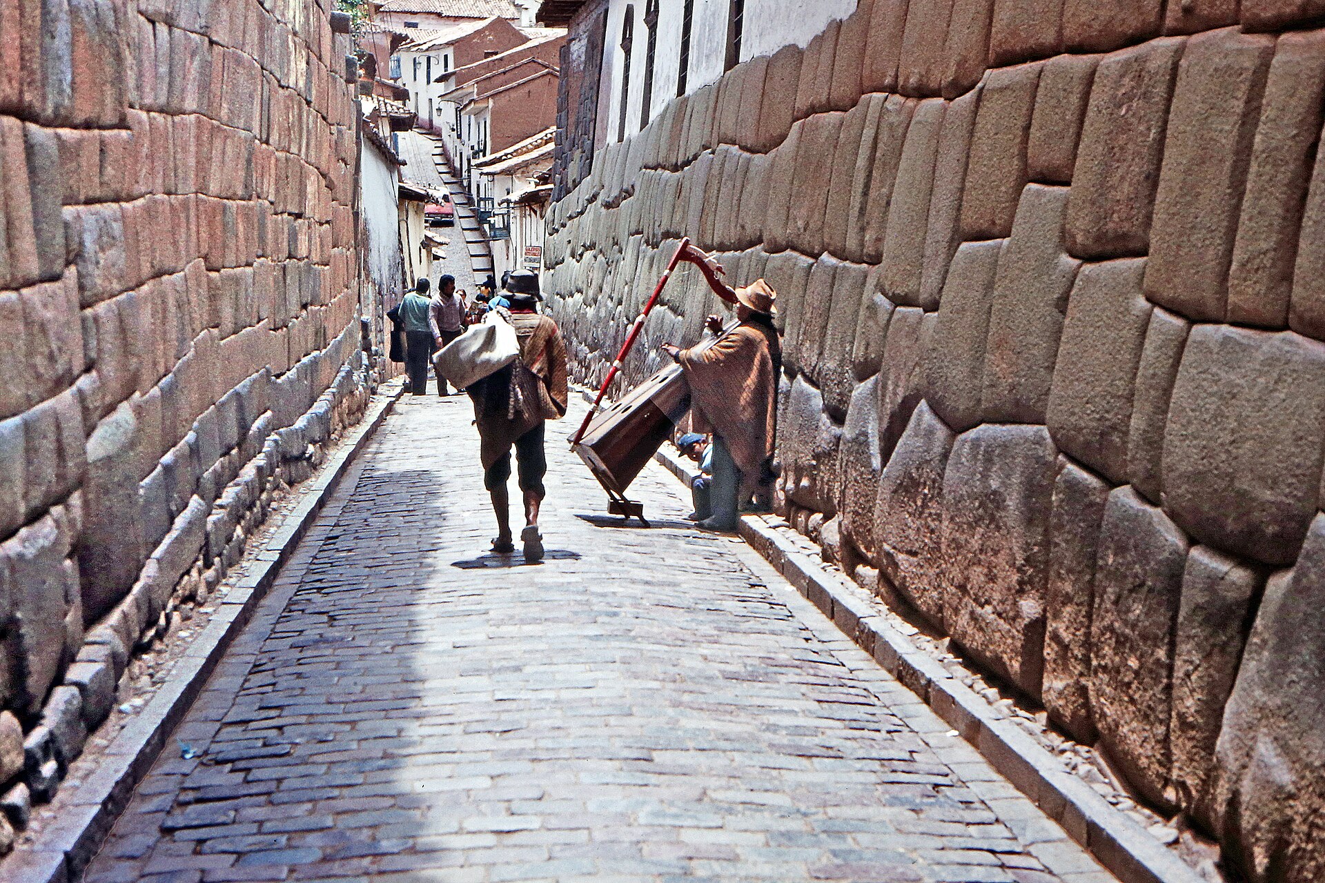 Two men walk along a cobbled lane between large fitted Inca stone walls in Cusco, Peru