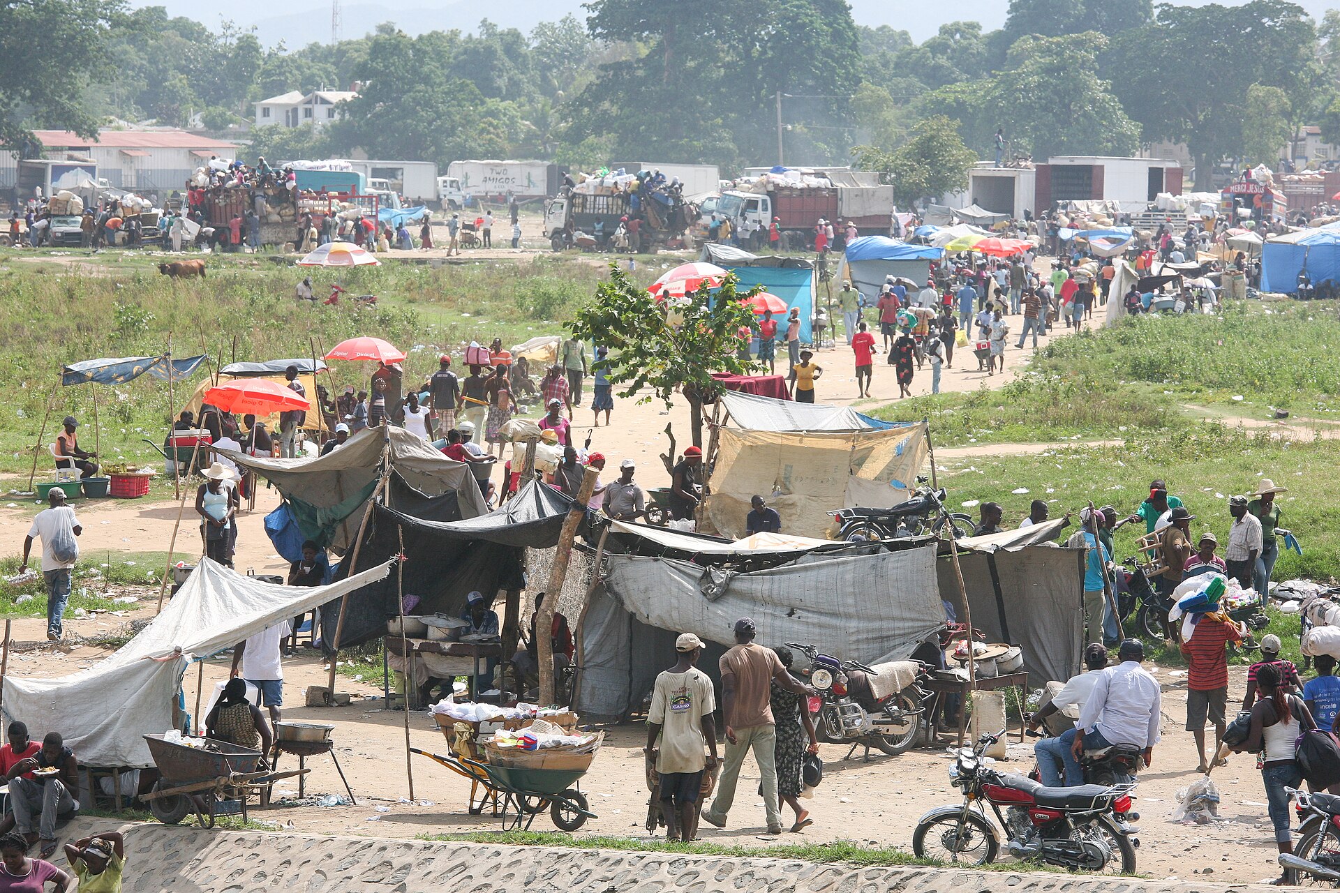 Crowds of people, stalls with tarpaulin roofs, motorbikes and loaded trucks at a busy border market on the Haiti and Dominican Republic frontier