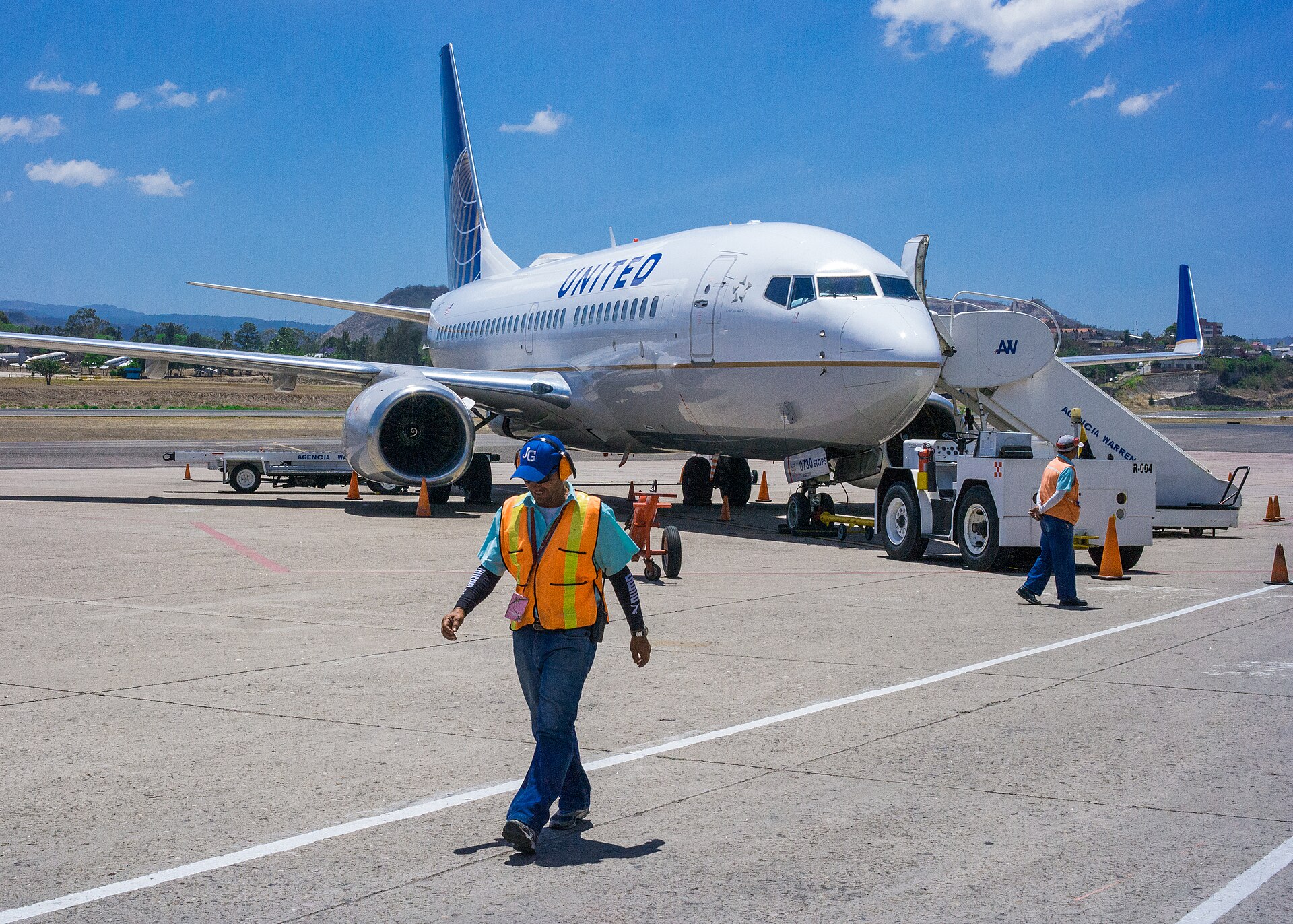 A United Airlines Boeing 737 parked on the apron at Toncontin airport with a ground worker in a high-visibility vest walking in front