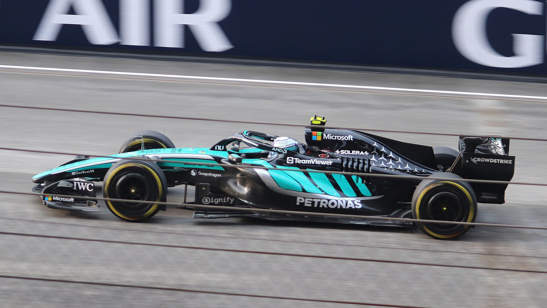 Teal and black Mercedes Formula 1 car passing an advertising board during a race