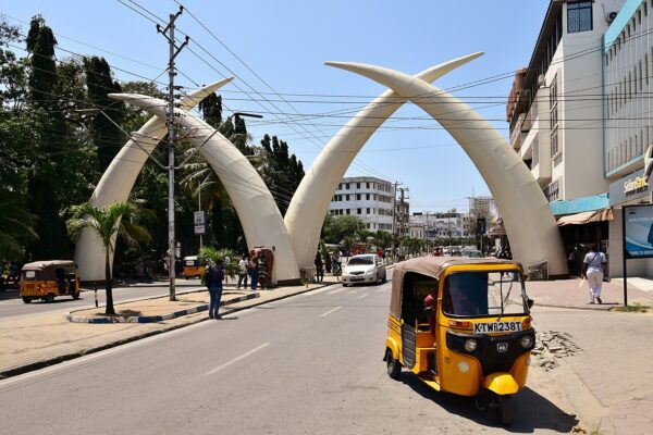 The crossed concrete tusks on Moi Avenue in Mombasa with a yellow tuk-tuk and a car in the street below.