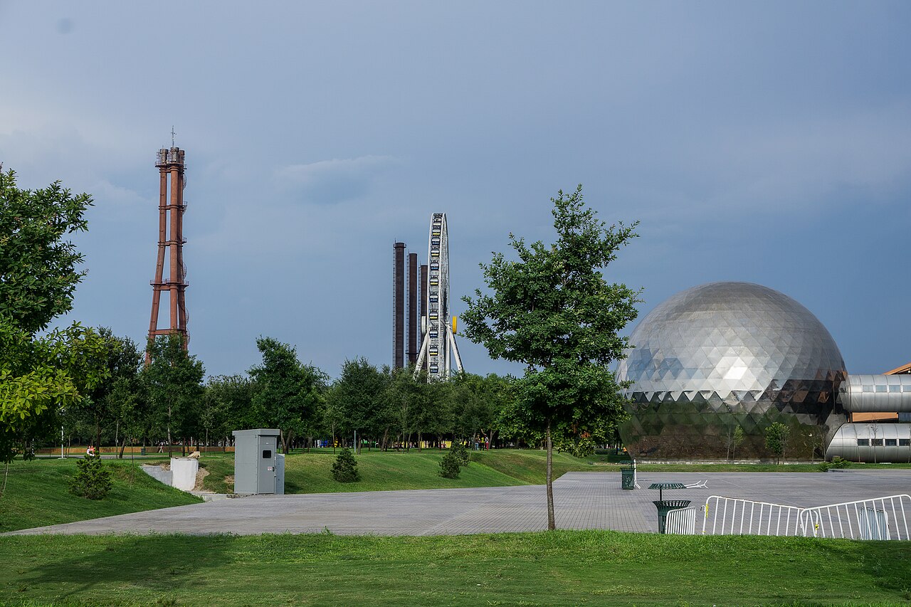 Chimneys, a Ferris wheel and a mirrored dome in Fundidora Park in Monterrey, Mexico, under a grey sky.