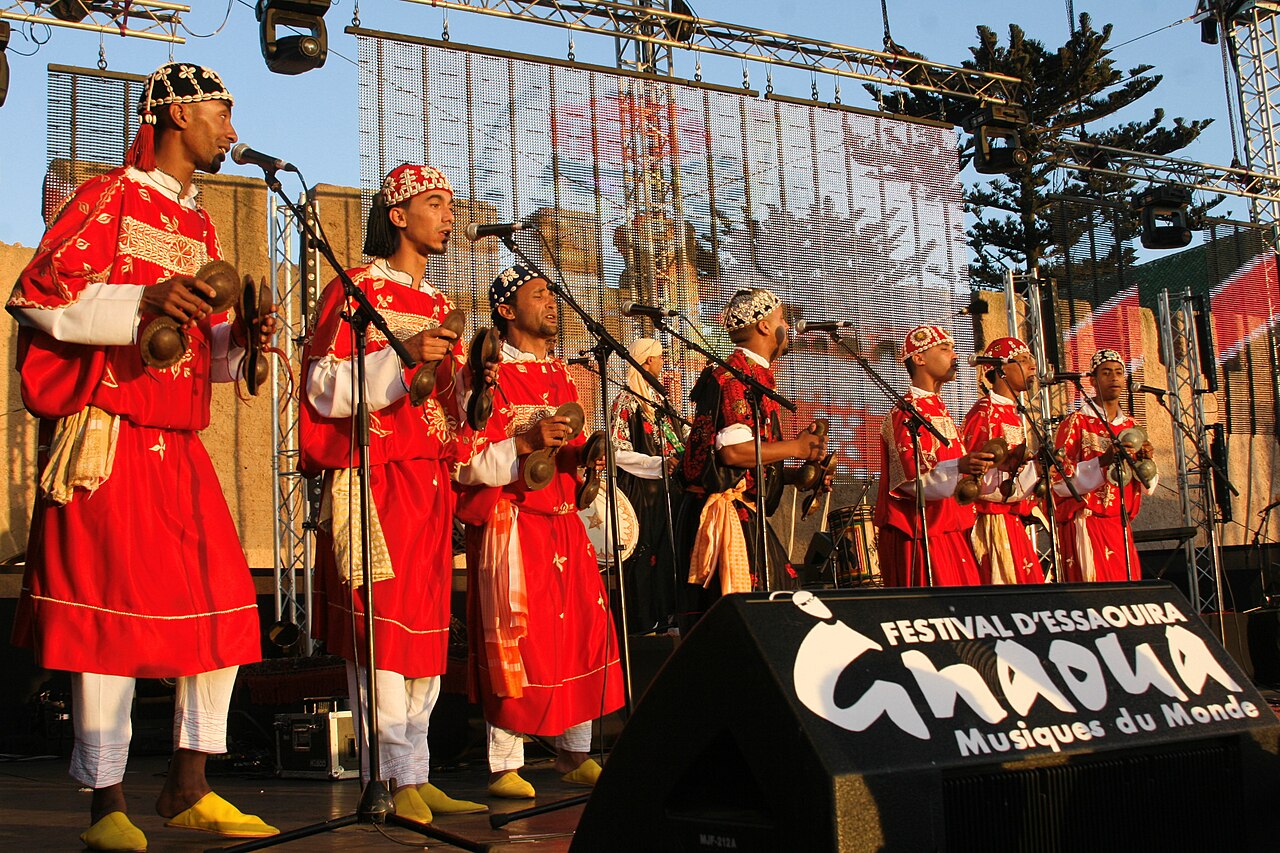 Gnawa musicians in red robes and embroidered caps play iron castanets on stage at the Gnaoua festival in Essaouira