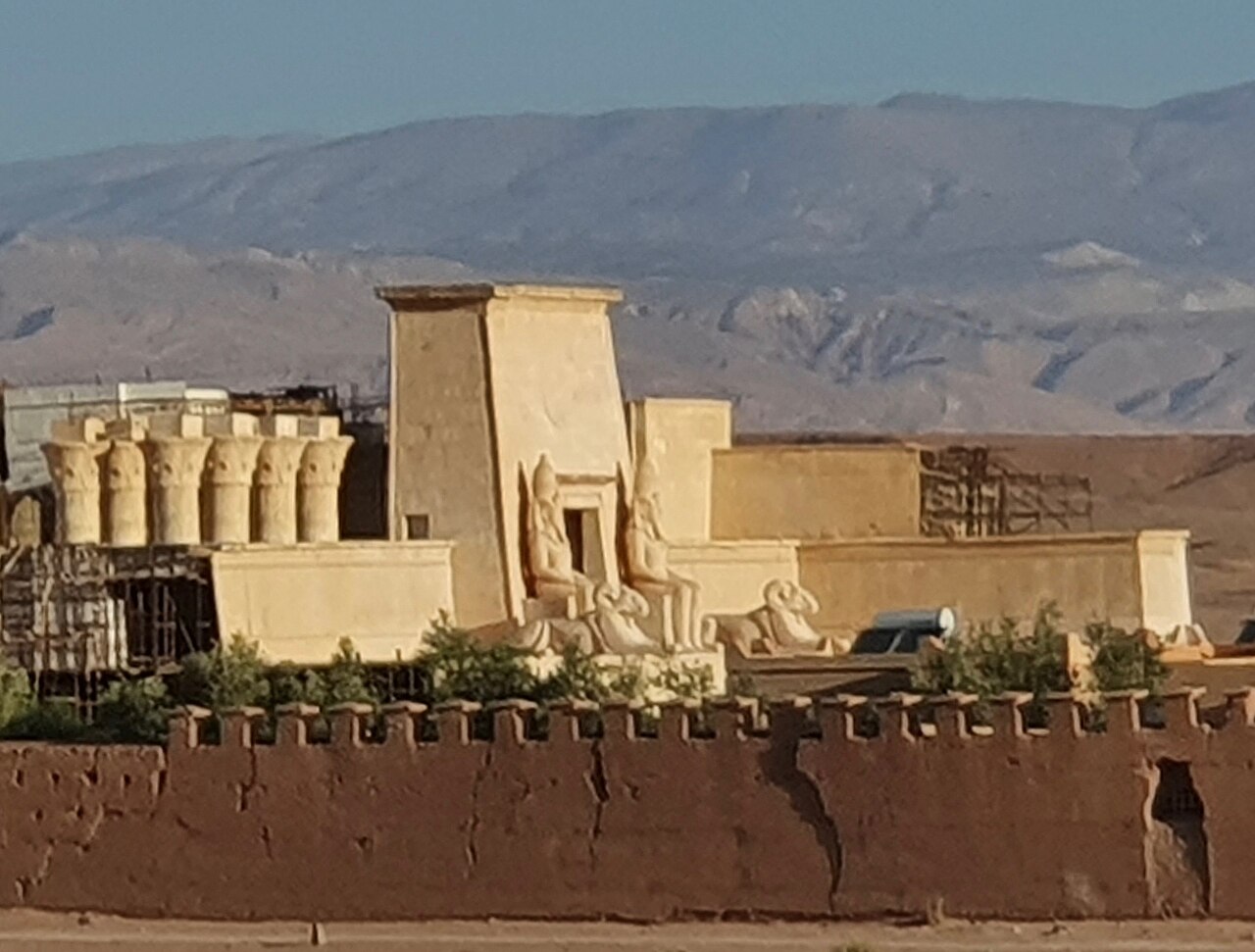 An Egyptian-style temple film set with pharaoh statues behind a mud-brick wall at a film studio in Ouarzazate, with mountains behind