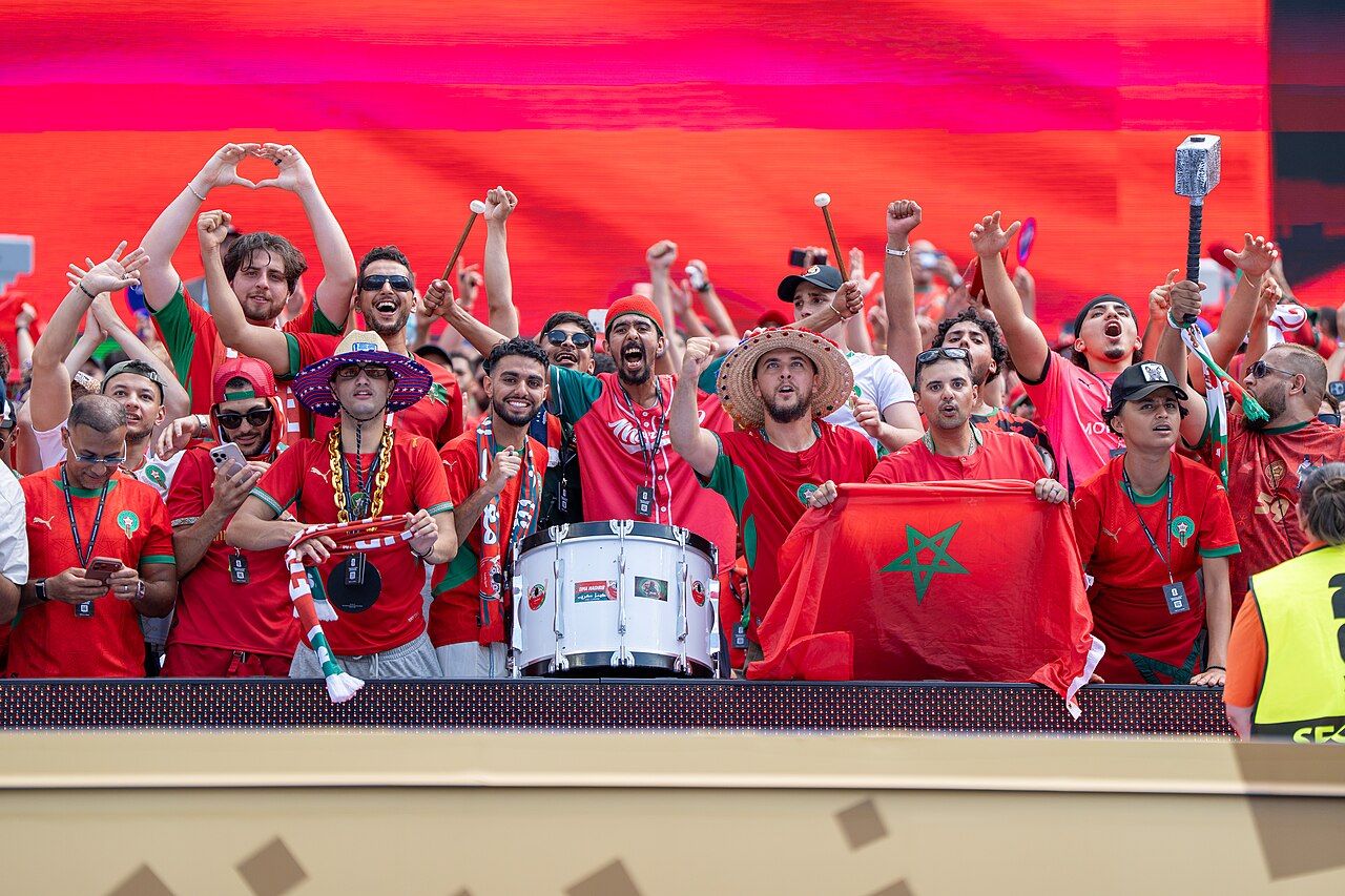 Morocco supporters in red shirts cheer with a drum and a Moroccan flag in the stands at the France v Morocco World Cup match