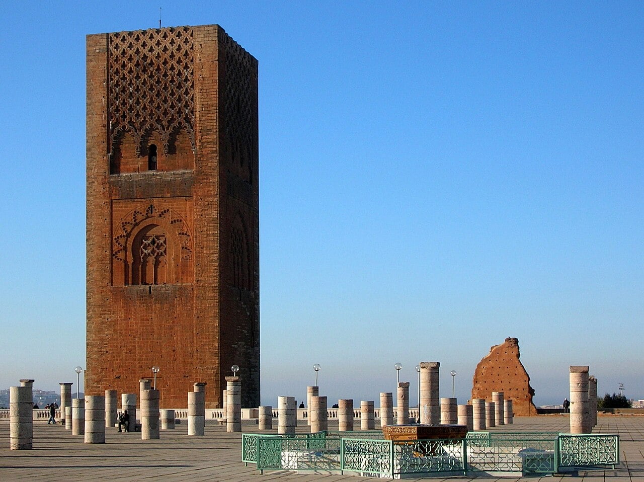 The Hassan Tower, a tall square reddish minaret, beside rows of stone columns under a clear blue sky in Rabat