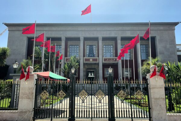 Front of the Moroccan Parliament building in Rabat, with red Moroccan flags and a wrought-iron gate