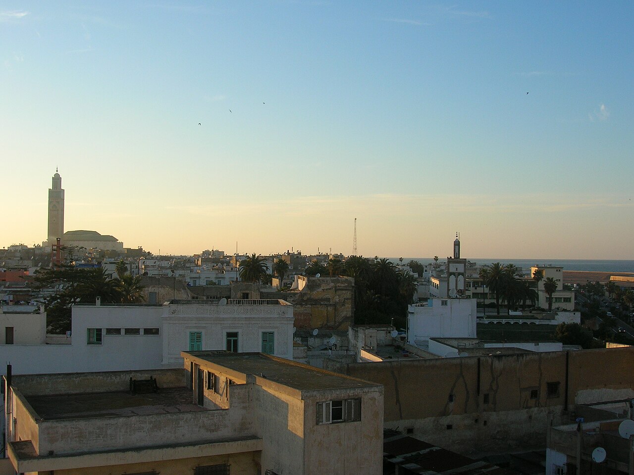 Rooftops of Casablanca at dusk, with the tall minaret of the Hassan II Mosque on the left and the Atlantic in the distance