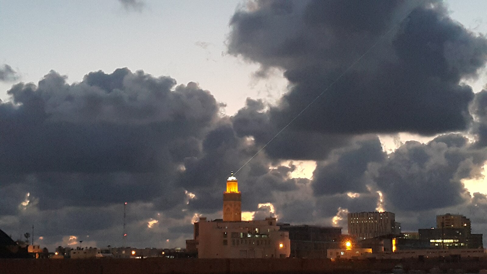 Morocco population and religion: a lit minaret above Casablanca at dusk
