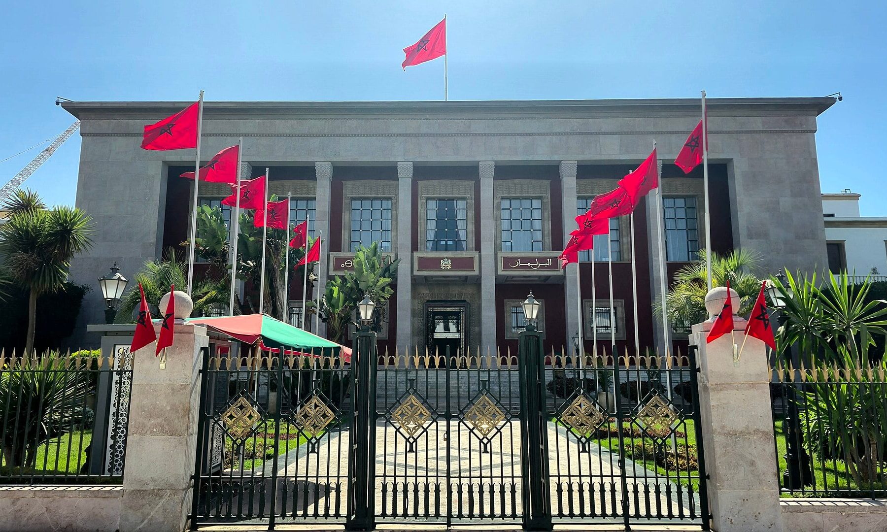 Front of the Moroccan Parliament building in Rabat, with red Moroccan flags and a wrought-iron gate