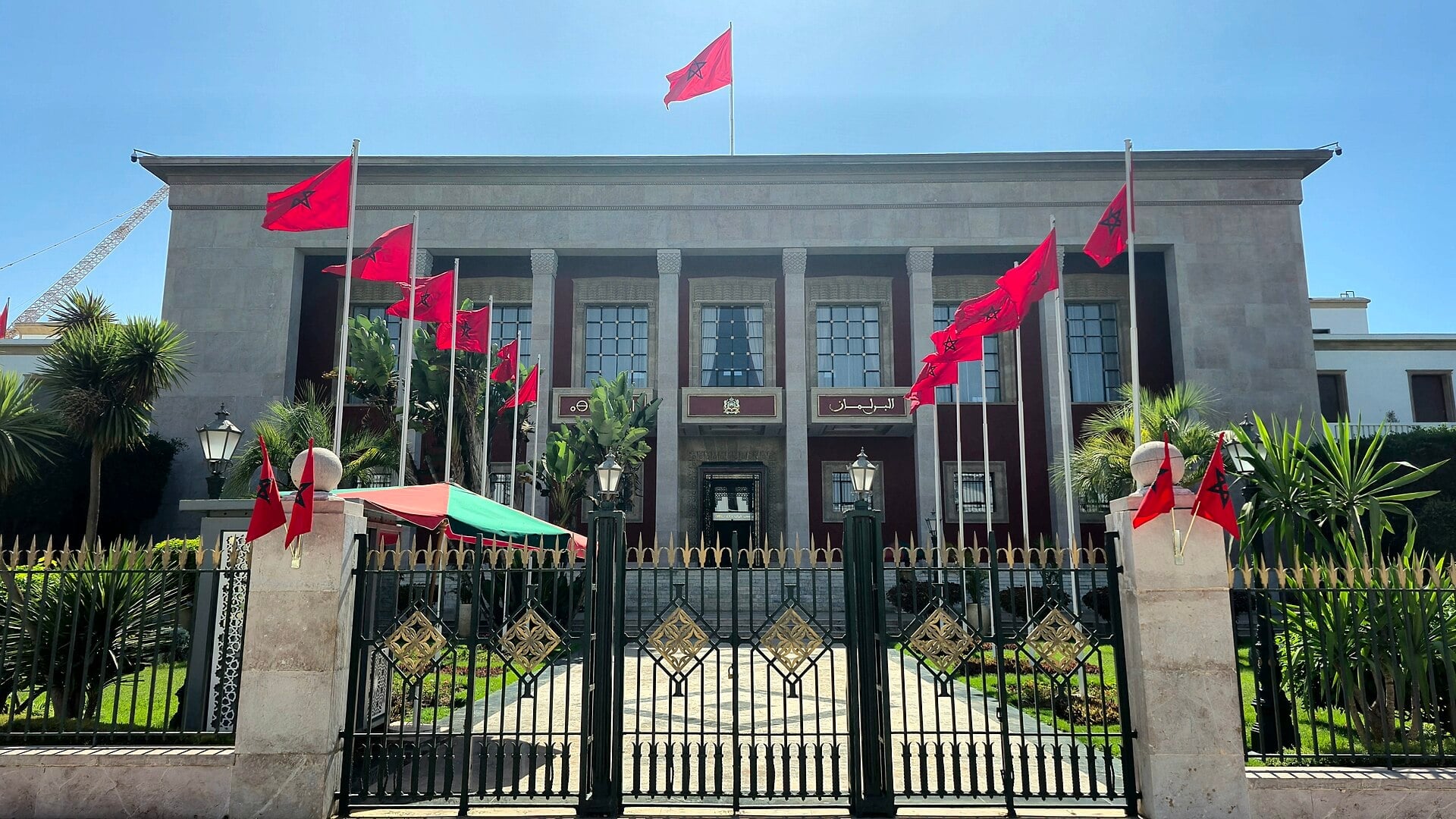 Front of the Moroccan Parliament building in Rabat, with red Moroccan flags and a wrought-iron gate