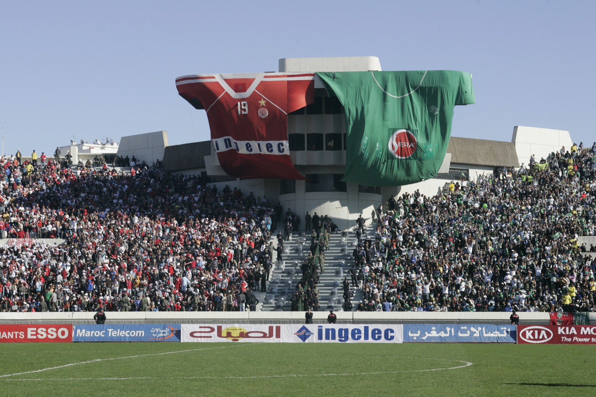 Packed football stands in Casablanca with fans of two clubs in red and green and two giant team shirts hung over the stadium tower
