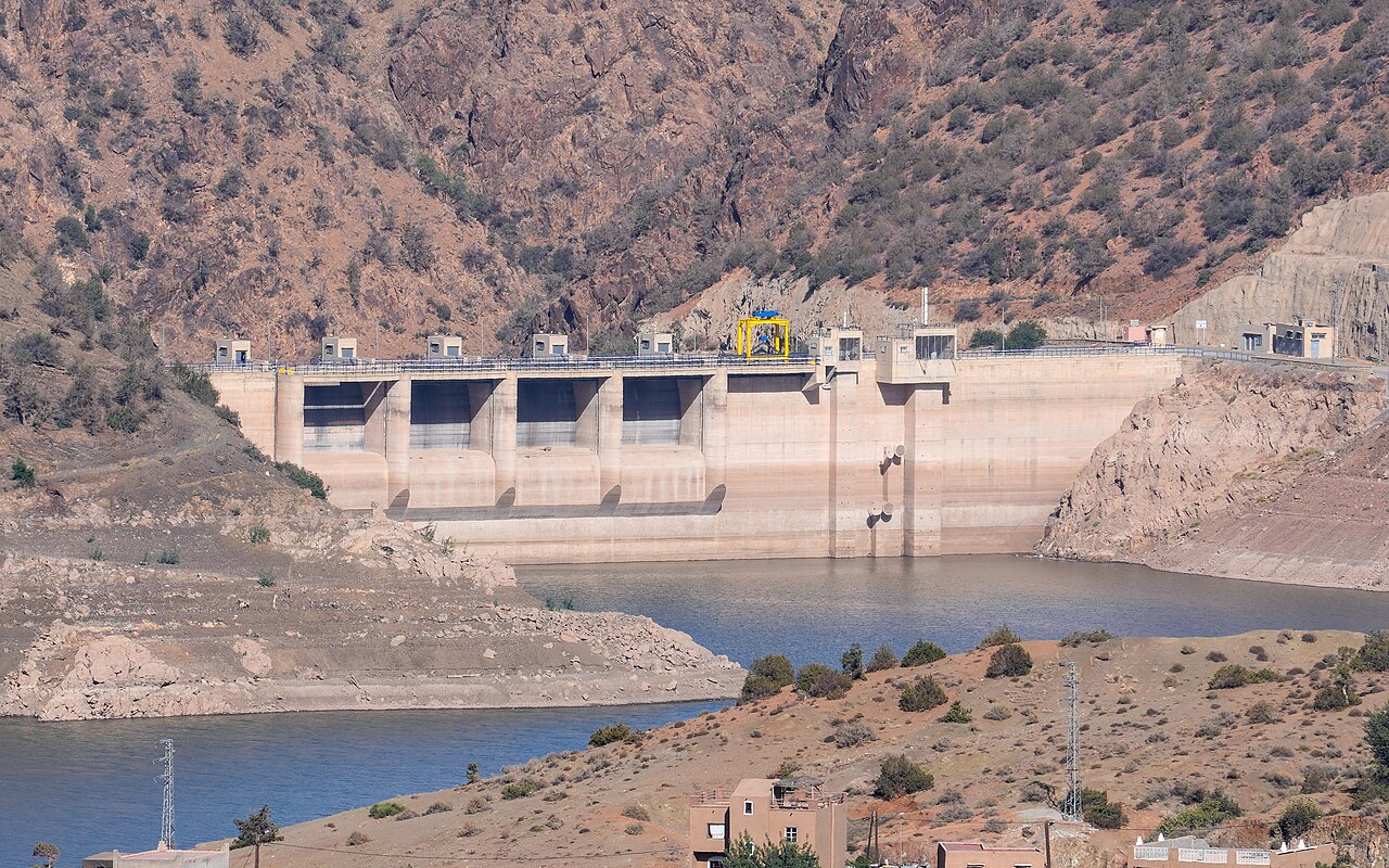 Yacoub el Mansour Dam in Morocco with a concrete spillway above a lake at low water and bare brown hills behind