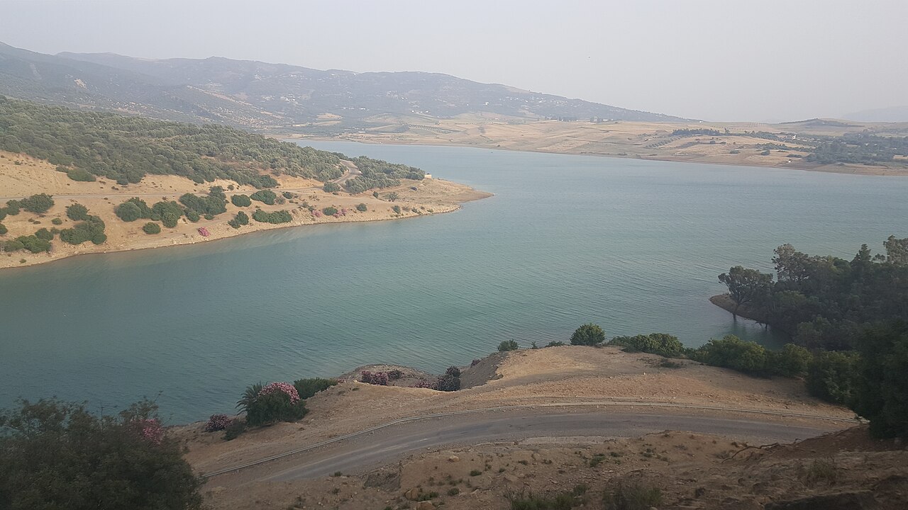 Blue-green reservoir lake with scrubby hills, olive groves and a winding road in northern Morocco