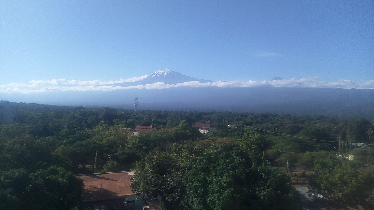 Rooftops and trees of Moshi town in Tanzania with Mount Kilimanjaro above a band of cloud.