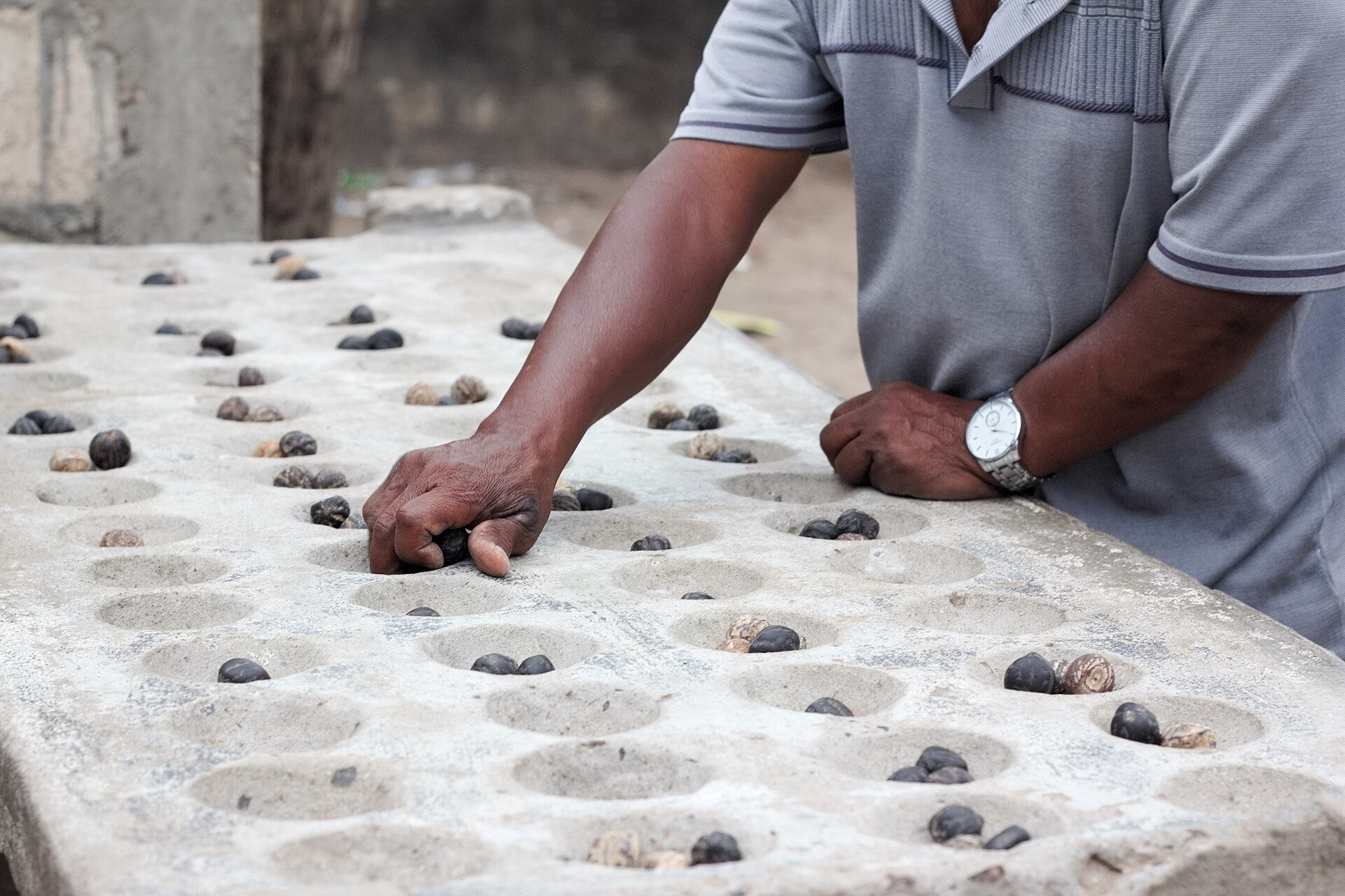 A man leans on a stone board with rows of hollows and dark seeds while playing a mancala-type game in Mafalala, Maputo