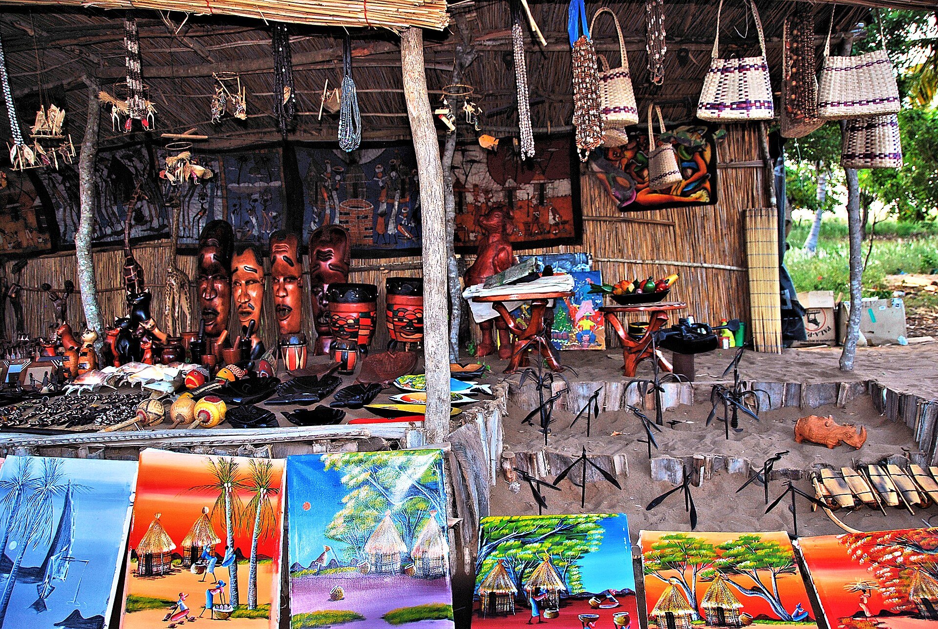Roadside craft stall in southern Mozambique with carved wooden masks, woven baskets, batik cloth and colourful paintings of village scenes