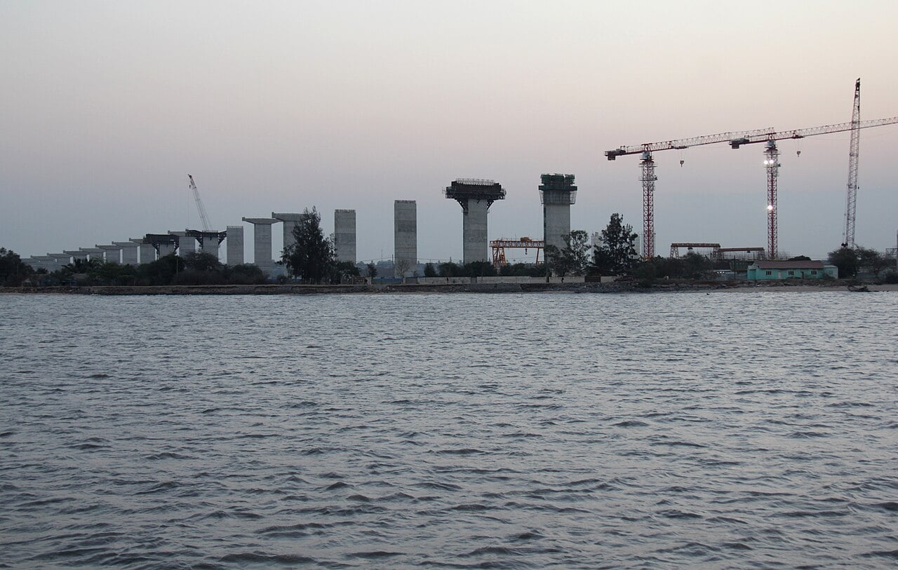 Concrete bridge pillars and tower cranes rising from the shore across the water at Maputo