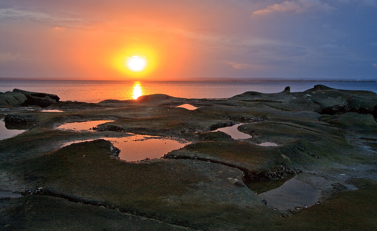 Sunset over Nacala Bay with tidal pools on dark rocks in the foreground