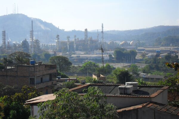 Refinery towers, pipes and storage tanks on a hazy hillside beyond houses and rooftops in Ibirité, Minas Gerais