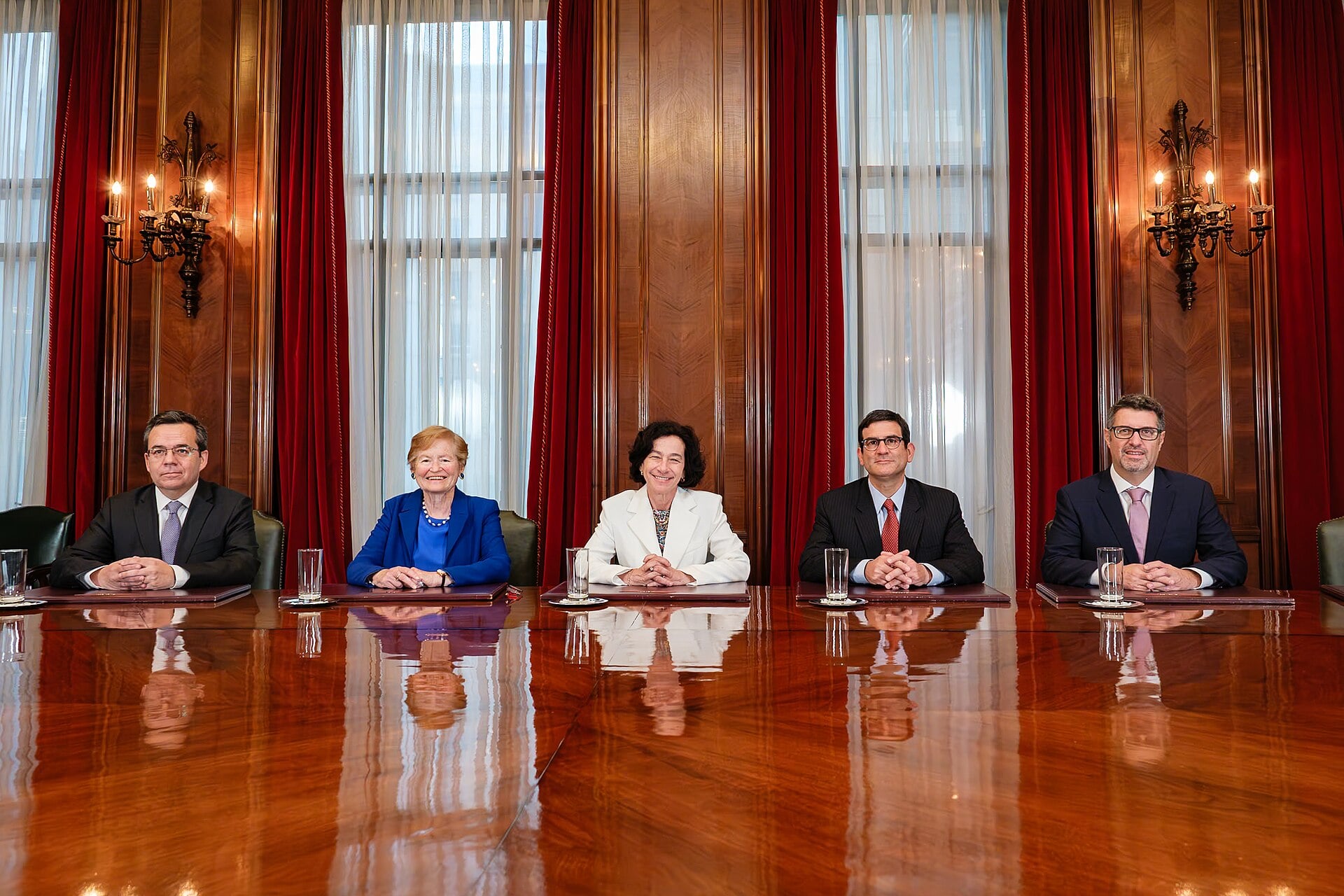 Five members of the Banco Central de Chile board seated at a long polished wooden table in a wood-panelled room with red curtains