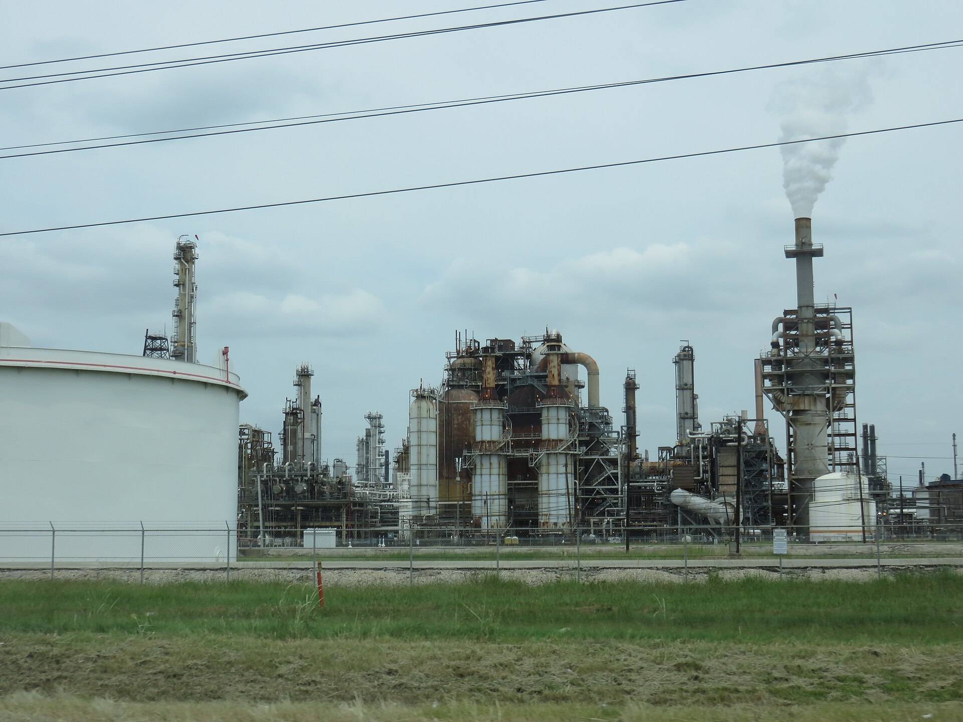 Towers, tanks and a smoking stack at an oil refinery behind a fence in Houston, Texas