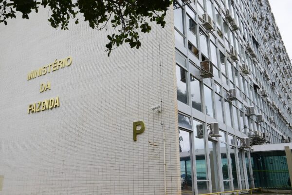 The white tiled Finance Ministry building on Brasília's Esplanada, with gold lettering reading Ministério da Fazenda and a large letter P, beneath tree branches