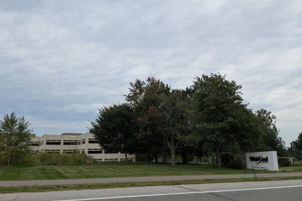 A low beige office building behind trees and a lawn, with a white Whirlpool sign at the roadside, under an overcast sky