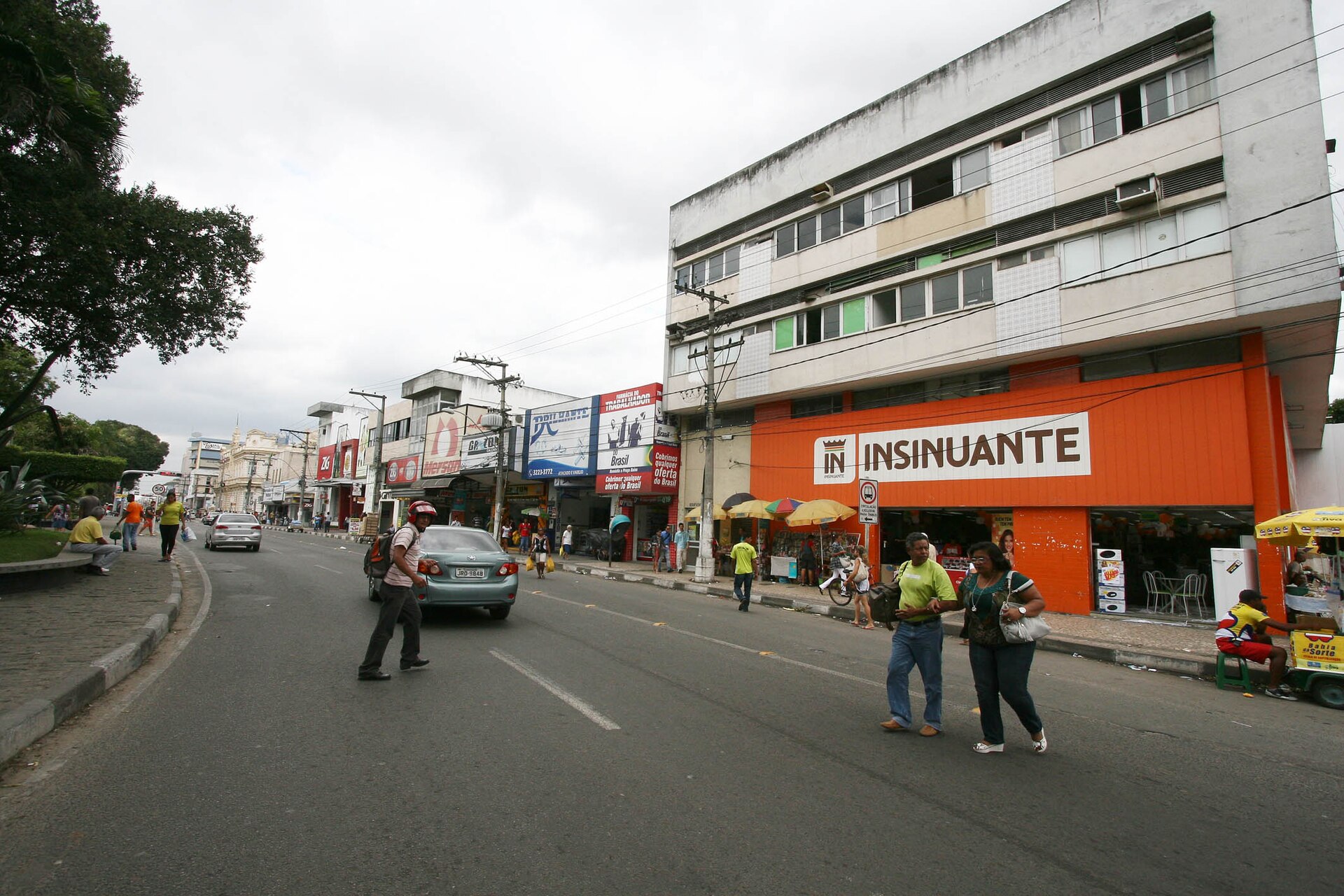 A street in Feira de Santana with pedestrians and a car in front of a three-storey building whose ground floor carries an orange Insinuante appliance store sign