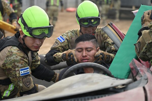 Three Salvadoran soldiers in camouflage, two in lime-green helmets and goggles, give first aid to a volunteer playing a trapped victim in a wrecked car