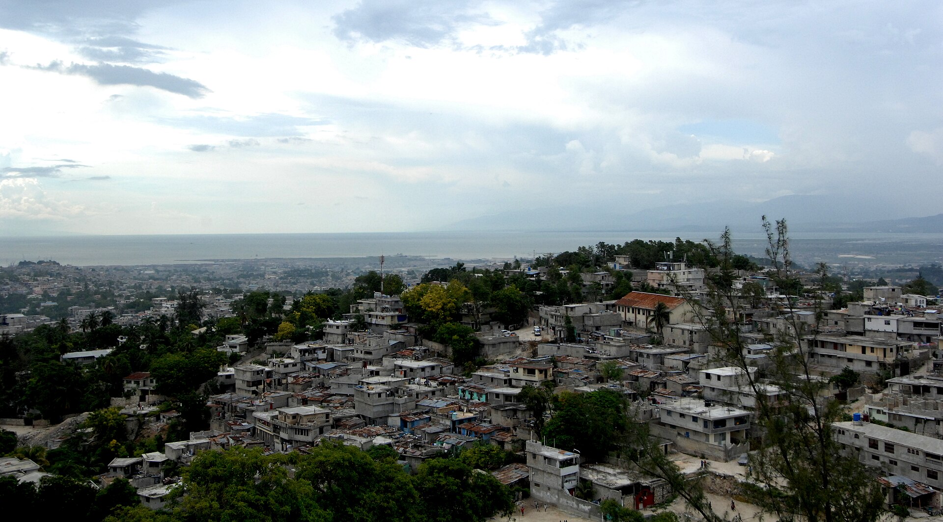 Hillside houses of Port-au-Prince under a cloudy sky with the bay and distant mountains behind