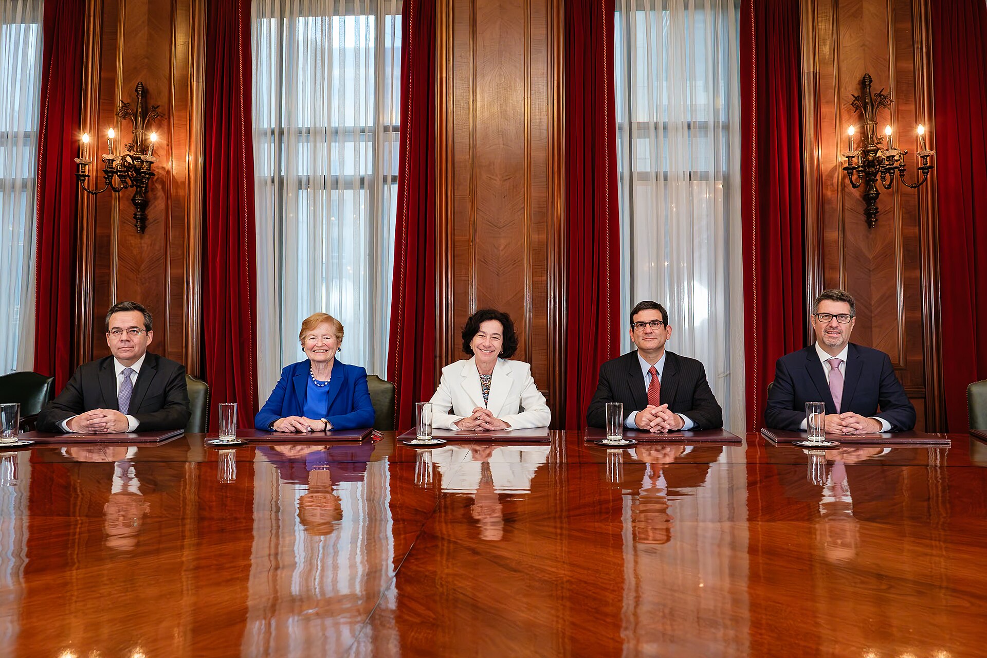 Five members of the Banco Central de Chile board seated at a long polished wooden table in a wood-panelled room with red curtains