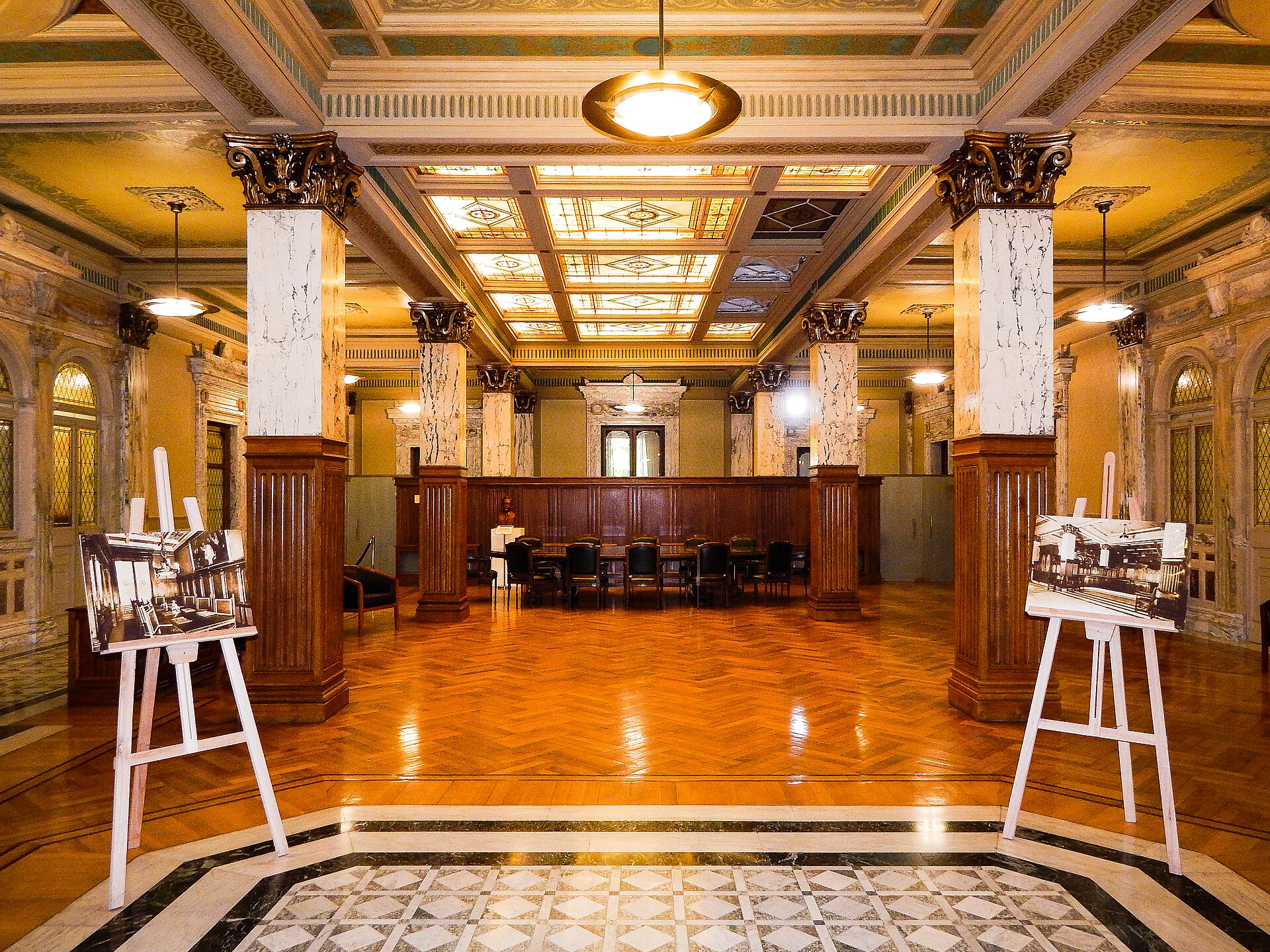 Marble-columned hall with a parquet floor, a long meeting table and two easels showing old photographs inside the AGN building
